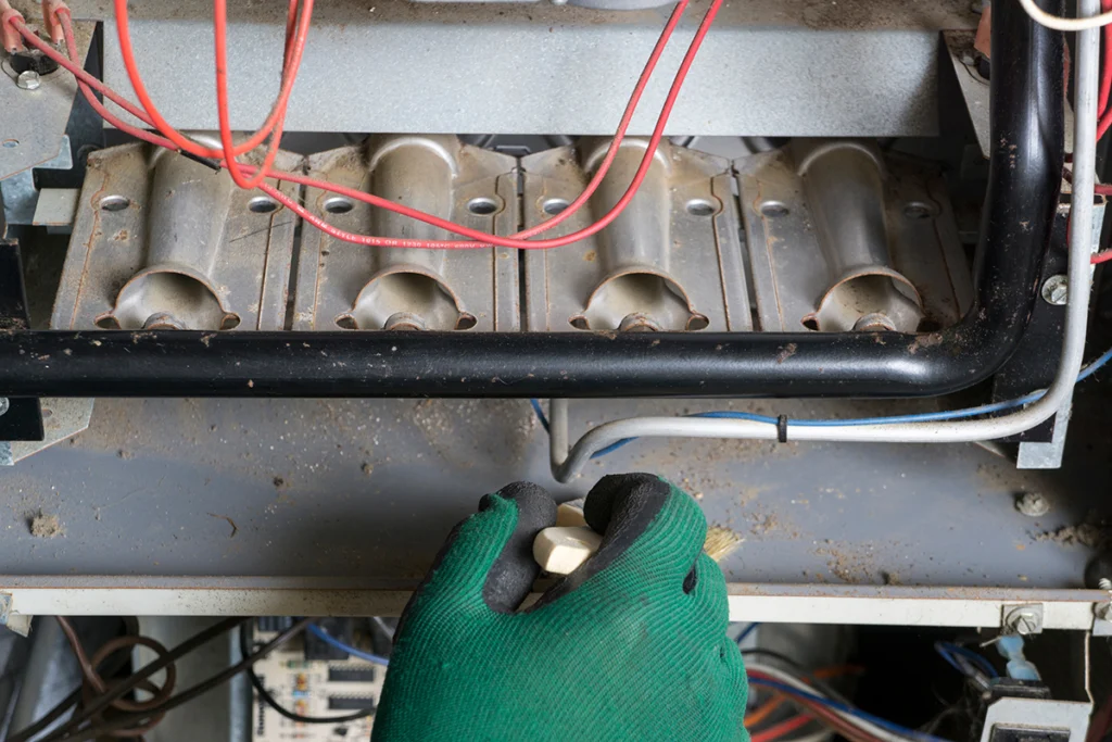 Technician inspecting the burner area of a furnace that supplies heat to the furnace heat exchanger