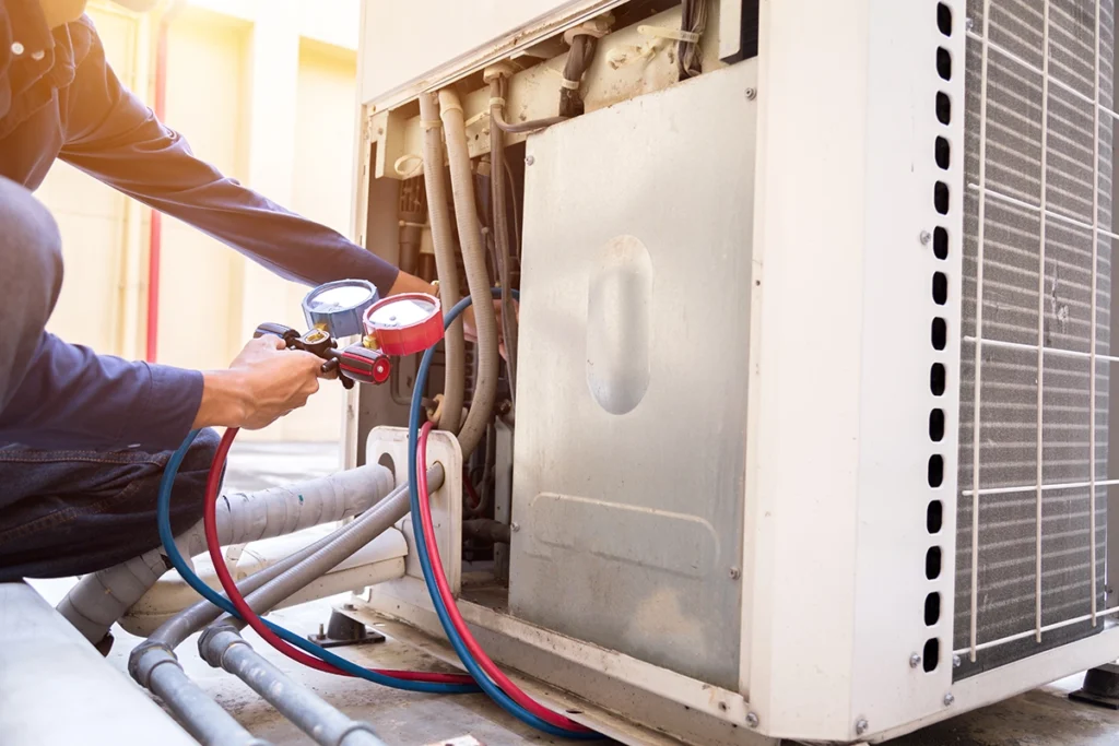 A technician measuring refrigerant pressure on an outdoor AC unit, inspecting essential parts of HVAC system equipment.