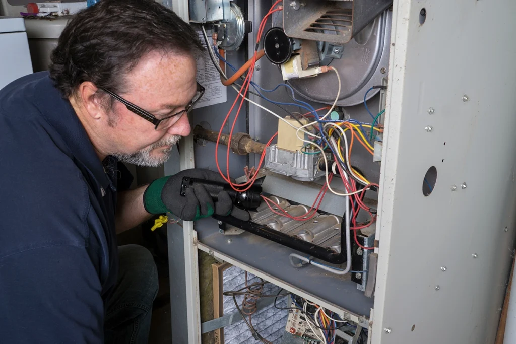 HVAC technician inspecting the internal gas valve and ignition components inside a furnace