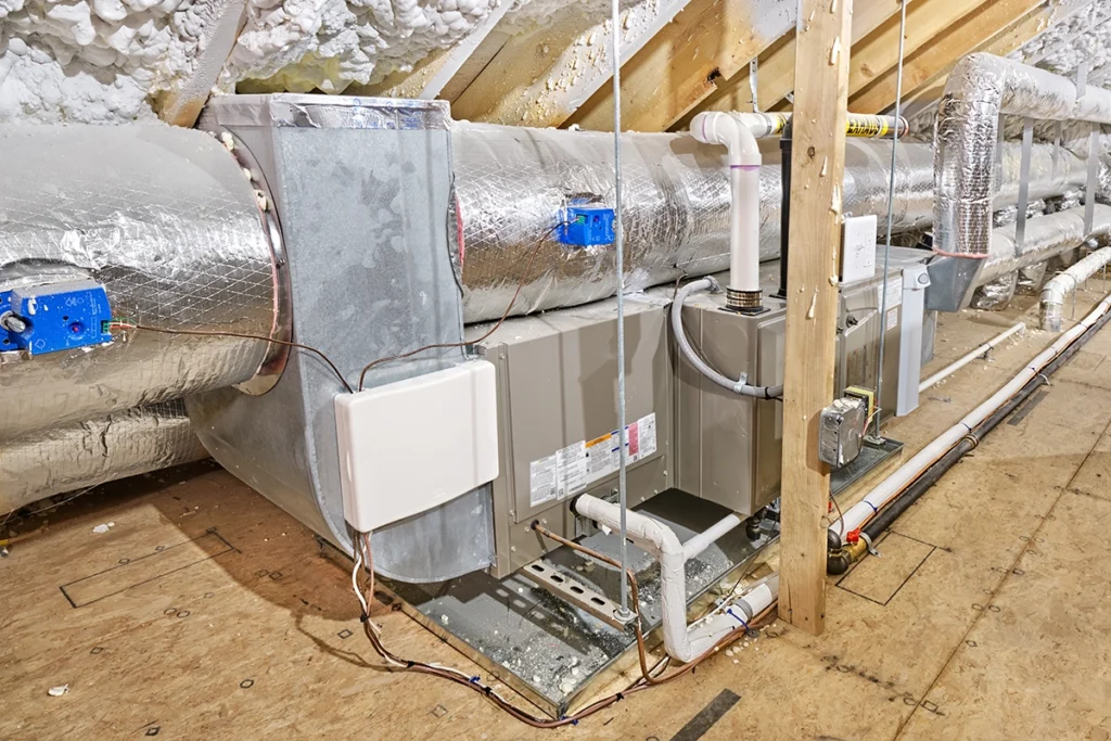 A high-efficiency furnace installed in an attic with insulated ductwork, PVC vent pipes, and connected drain lines.