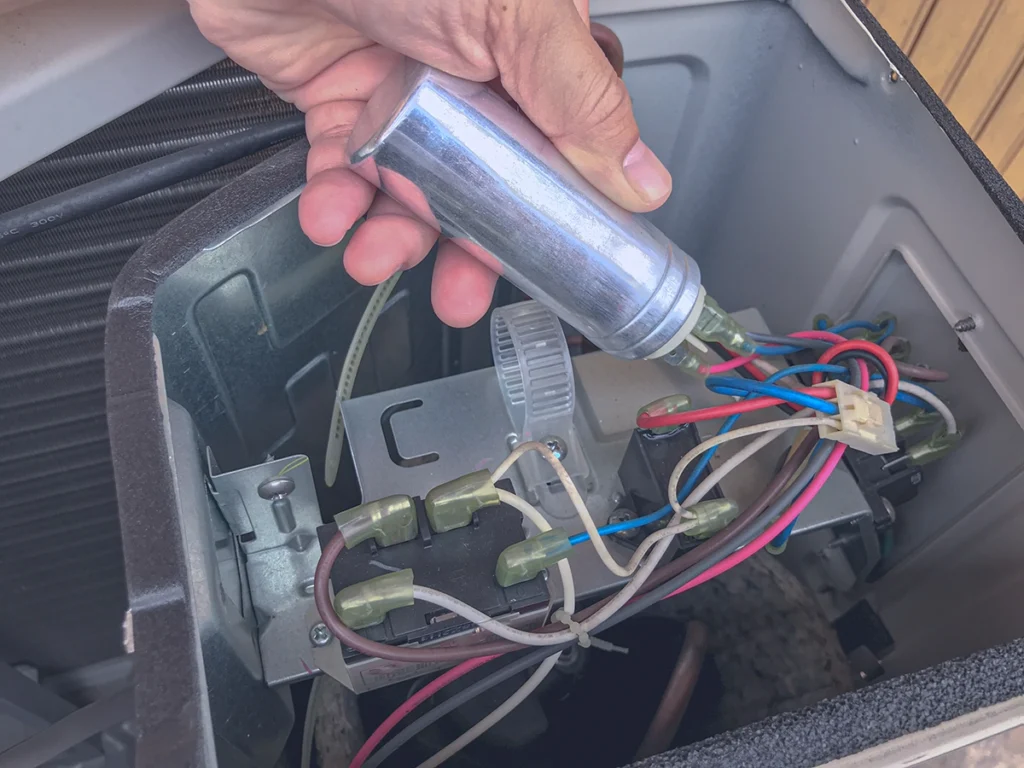 Technician holding an hvac capacitor inside an outdoor AC unit during repair service