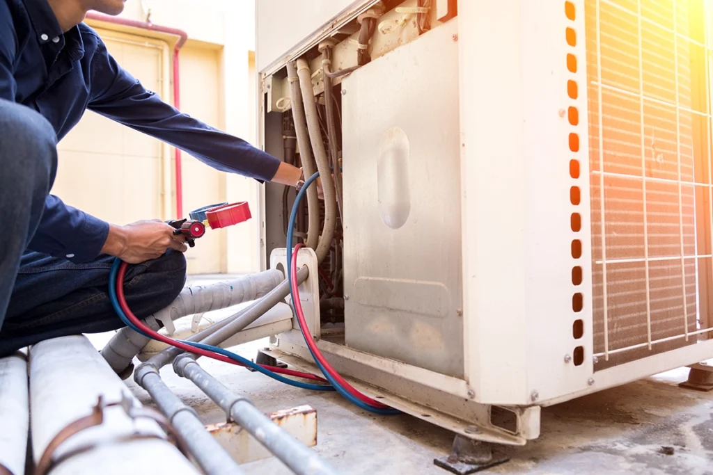 Technician servicing an outdoor HVAC unit and checking refrigerant lines during an R454B refrigerant system inspection