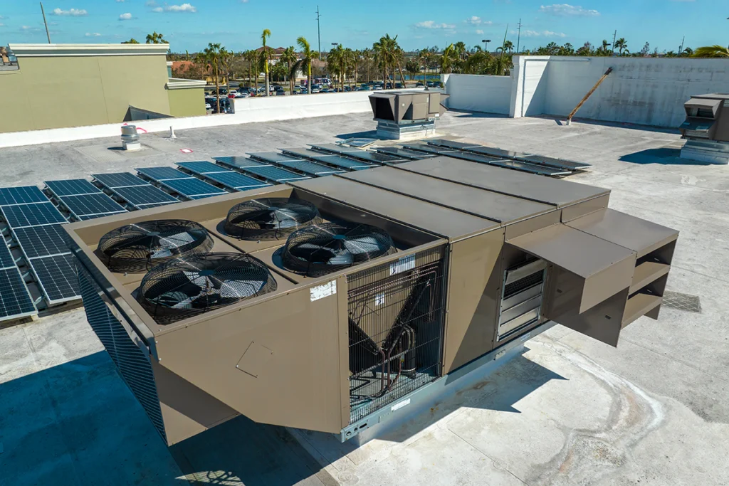 Commercial rooftop economizer HVAC system installed on a flat roof beside solar panels at a large facility.