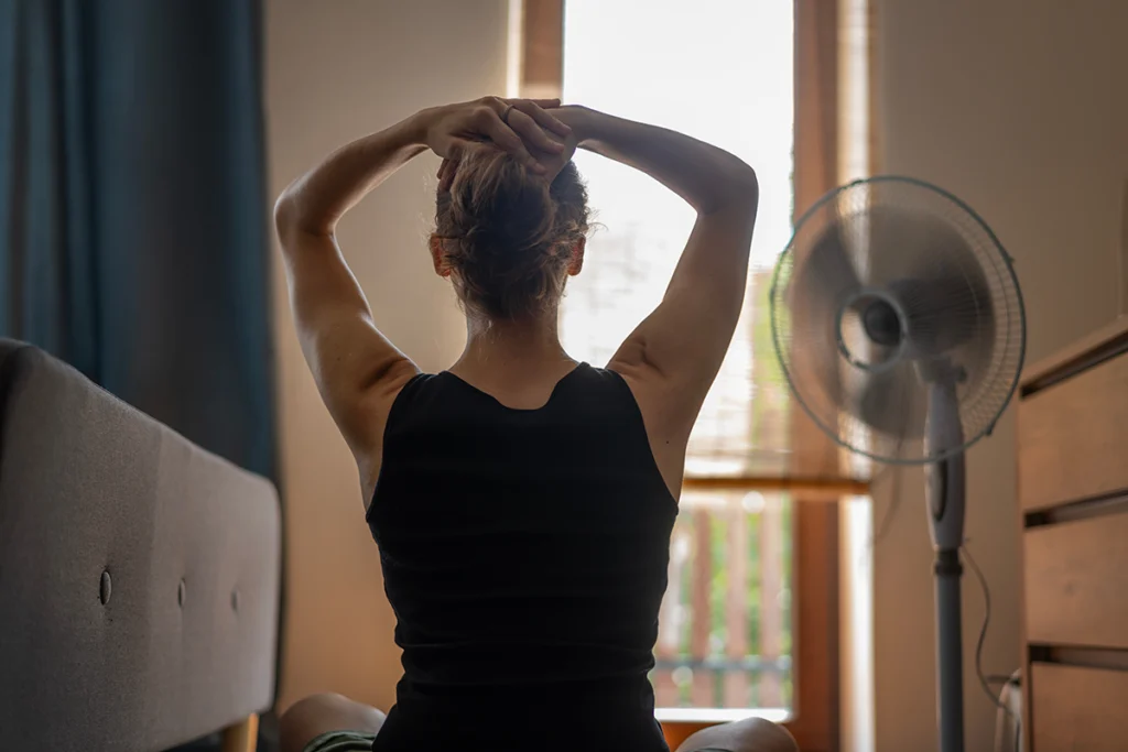 Homeowner sitting beside a fan in a warm room while dealing with an AC not blowing cold air.