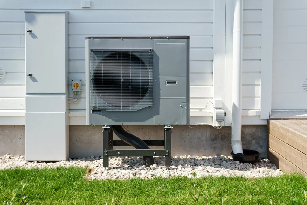 An outdoor heat pump condenser unit mounted on a concrete pad with gravel base next to a residential foundation. Best for blogs about heat pump systems, ductless outdoor units, heat pump installation, heat pump replacement, energy-efficient heating and cooling, and outdoor HVAC equipment.