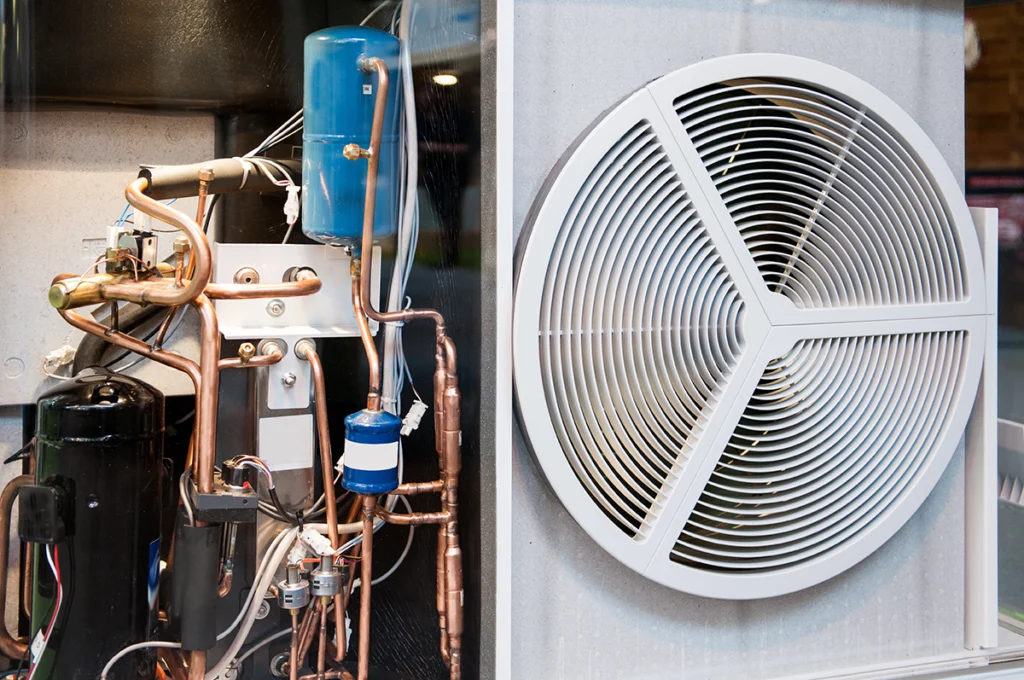 Interior view of a heat pump unit with visible refrigerant lines, compressor, and fan assembly.