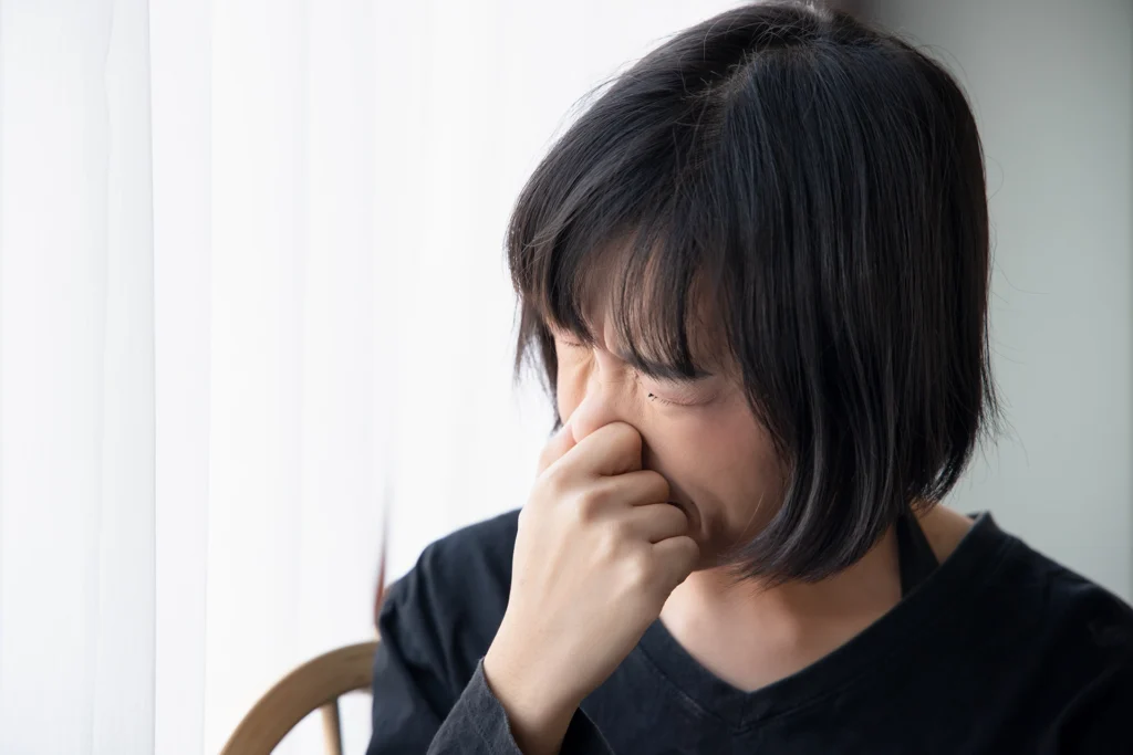 Person covering their nose indoors to represent poor indoor air quality or unpleasant indoor odors. Best for blogs about bad smells from vents, why does my house smell weird when the heat turns on, indoor air quality problems, musty AC smell, dirty sock syndrome, and odor-related HVAC issues.