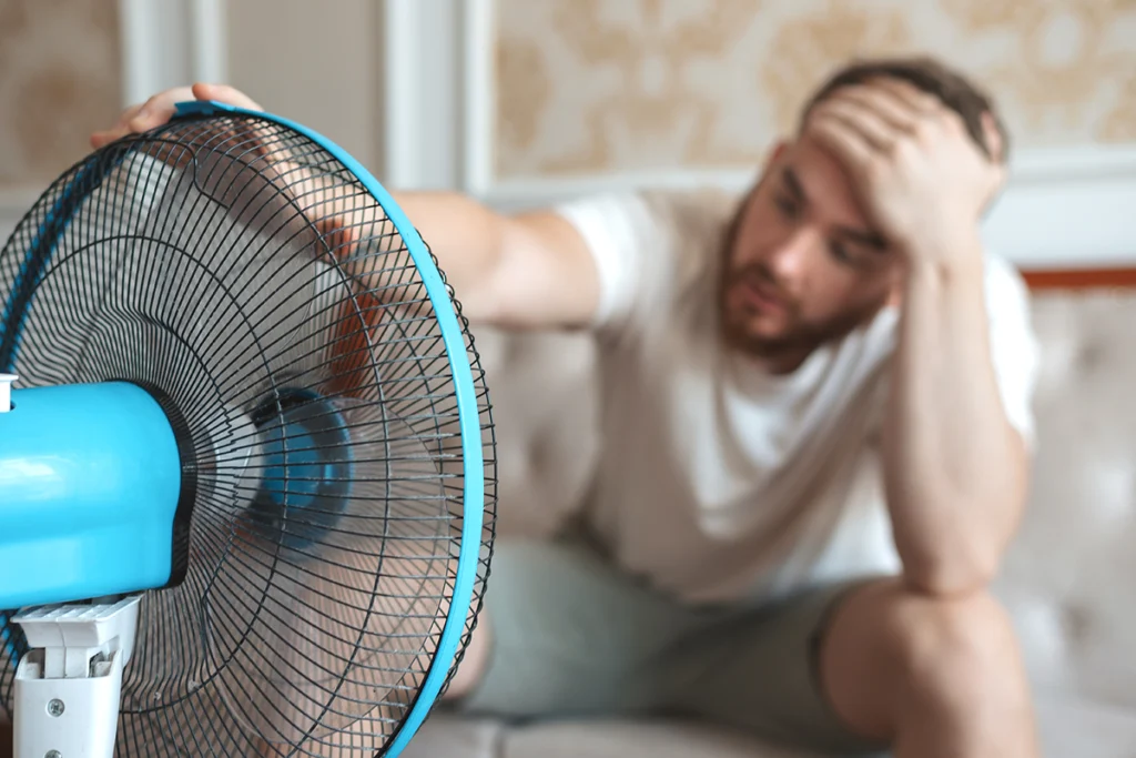 Man using a fan because of an air conditioner refrigerant leak causing weak cooling in Athens.